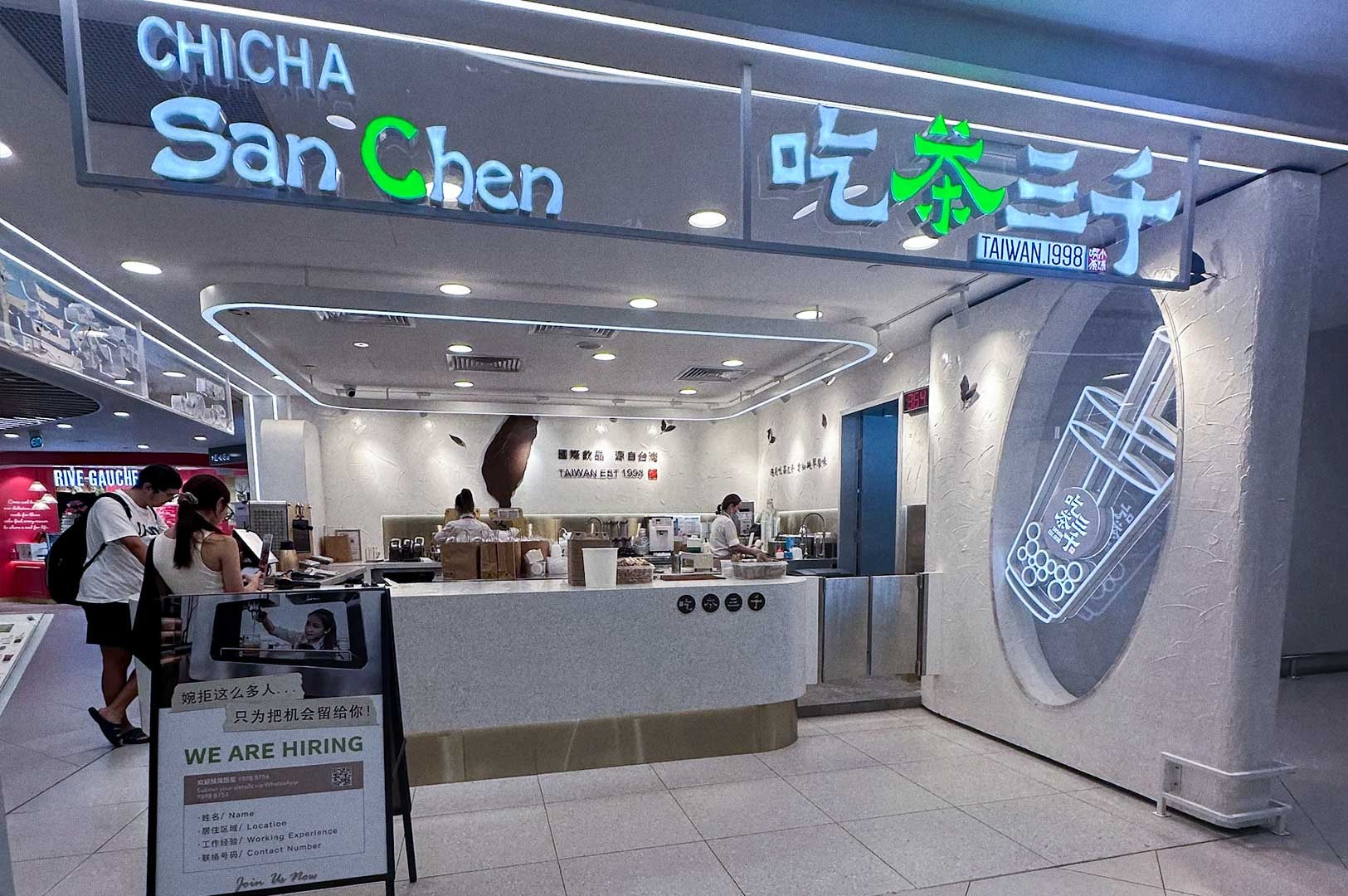 Front view of CHICHA San Chen bubble tea shop in a mall, with illuminated English and Chinese signage, a neon bubble‑tea cup on the wall.