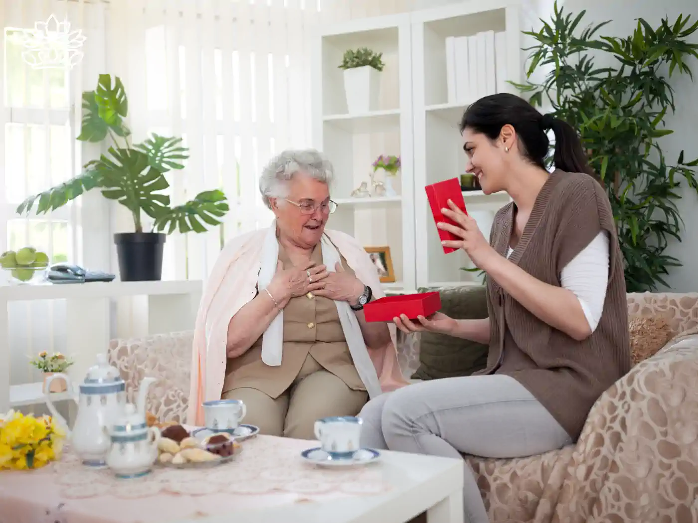 Elderly woman being presented with a retirement gift box by a younger woman in a cozy setting. Fabulous Flowers and Gifts. Retirement Gift Boxes.