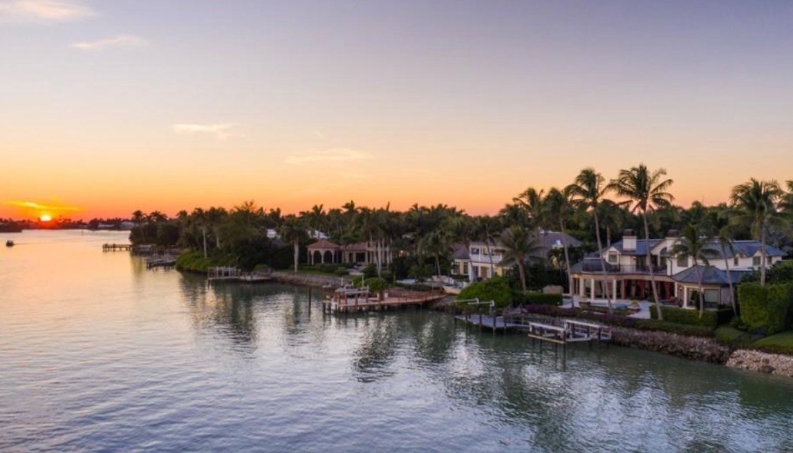 An aerial view showcases the prestigious Port Royal neighborhood in Naples, FL, featuring stunning waterfront estates with luxury yachts docked along pristine canals, embodying unparalleled beachfront retreat and resort-style living. The image highlights the serene waterfront views and expansive outdoor living spaces that characterize these exquisite properties.
