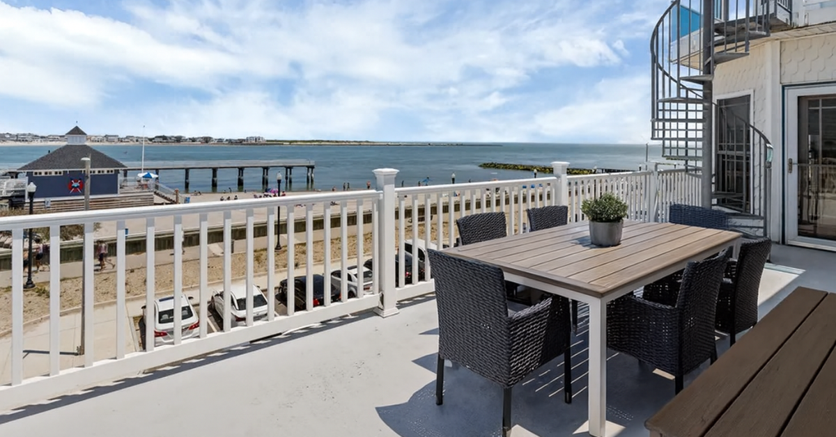 A large waterfront deck with outdoor dining furniture overlooking the bay, pier, and beach in Atlantic City.