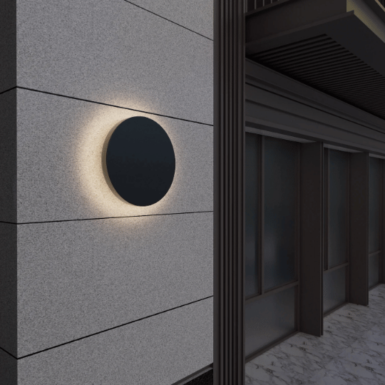 Modern circular black wall light mounted on a textured exterior wall, creating a soft, halo-like glow around the fixture near a building entrance.