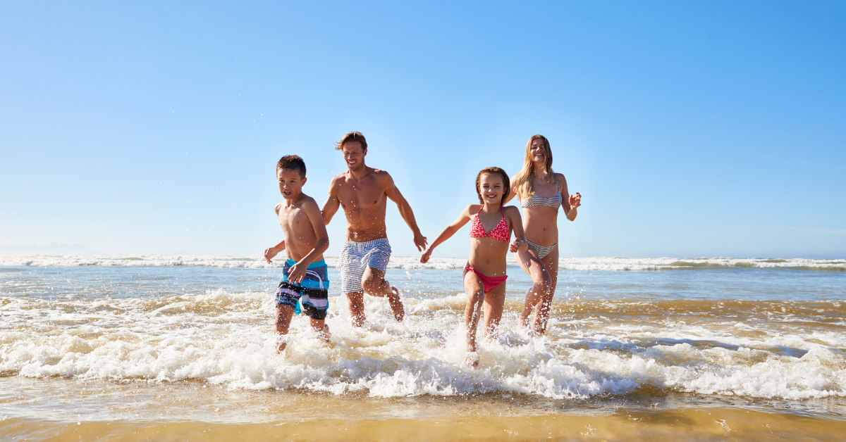 Family with two children running through ocean waves on a sunny day in the Wildwoods, enjoying a summer beach vacation on the Jersey Shore.