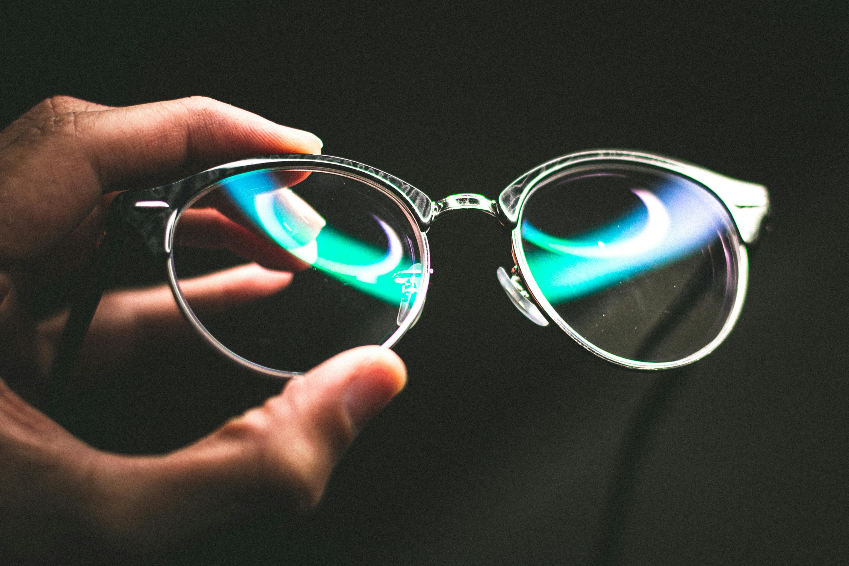 Hand holding glasses with reflection on lens against a black background