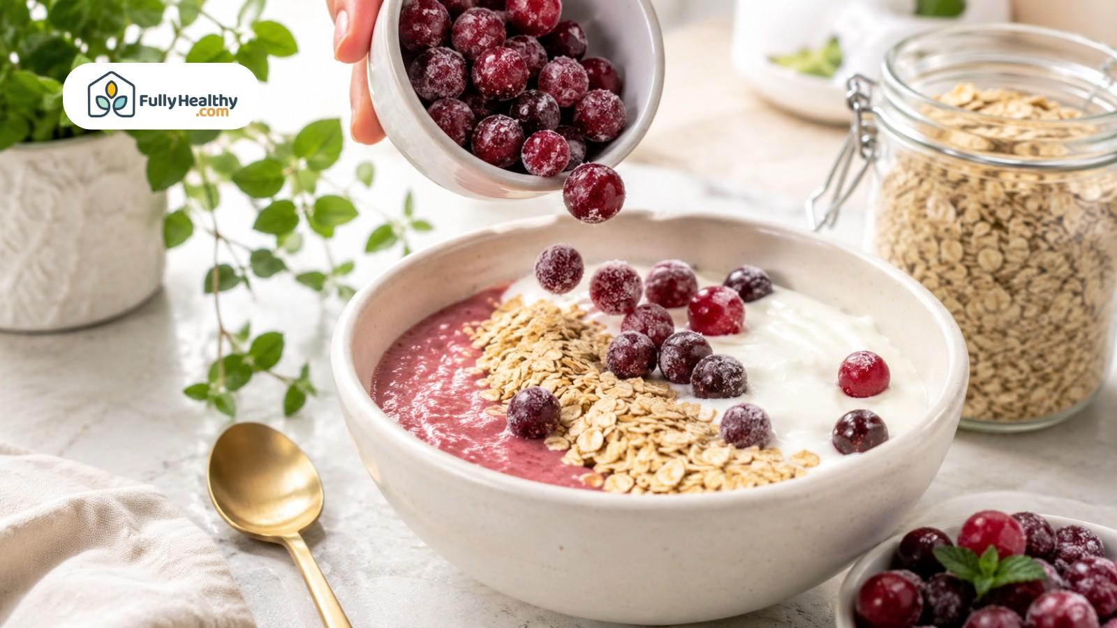 Frozen cranberries added to smoothie bowl with oats and creamy yogurt