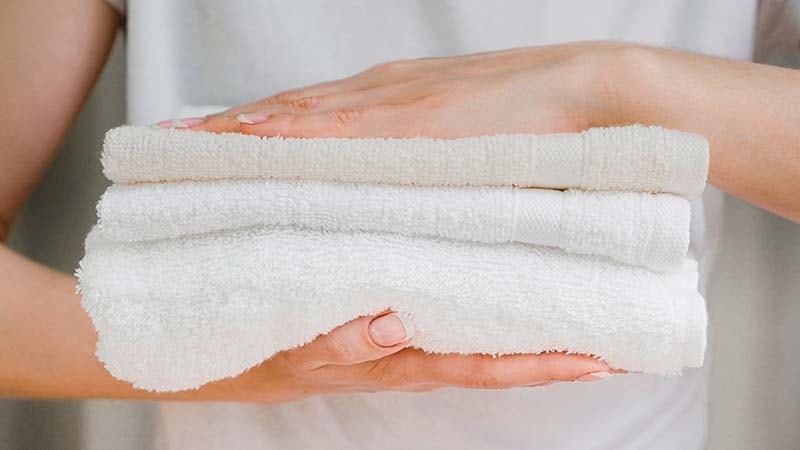 a woman holding a stack of freshly cleaned towels