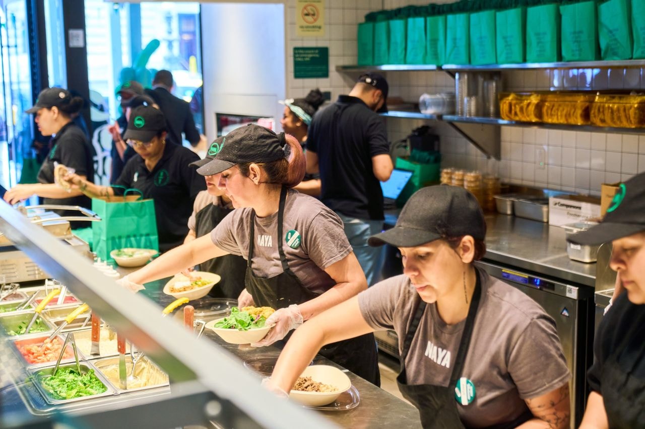 Naya team members serving salad at Naya's Bryant Park restaurant location. In frame is lettuce and other veggie toppings