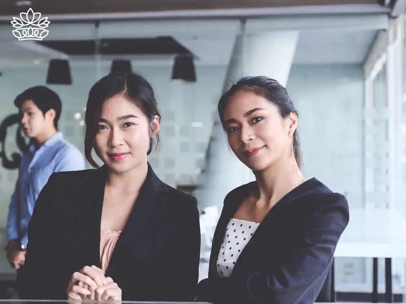 Confident young Asian businesswomen posing in a modern office environment, demonstrating professionalism and teamwork with a colleague in the background. Fabulous Flowers and Gifts - Gift Boxes for Clients. Delivered with Heart