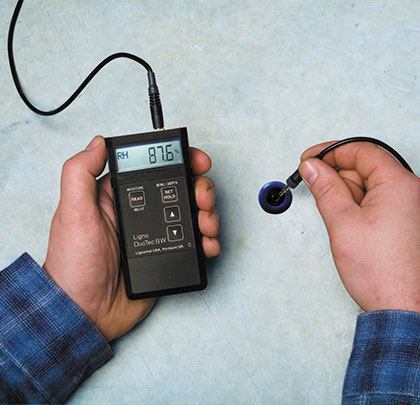 A person measuring moisture in a concrete subfloor with a moisture meter