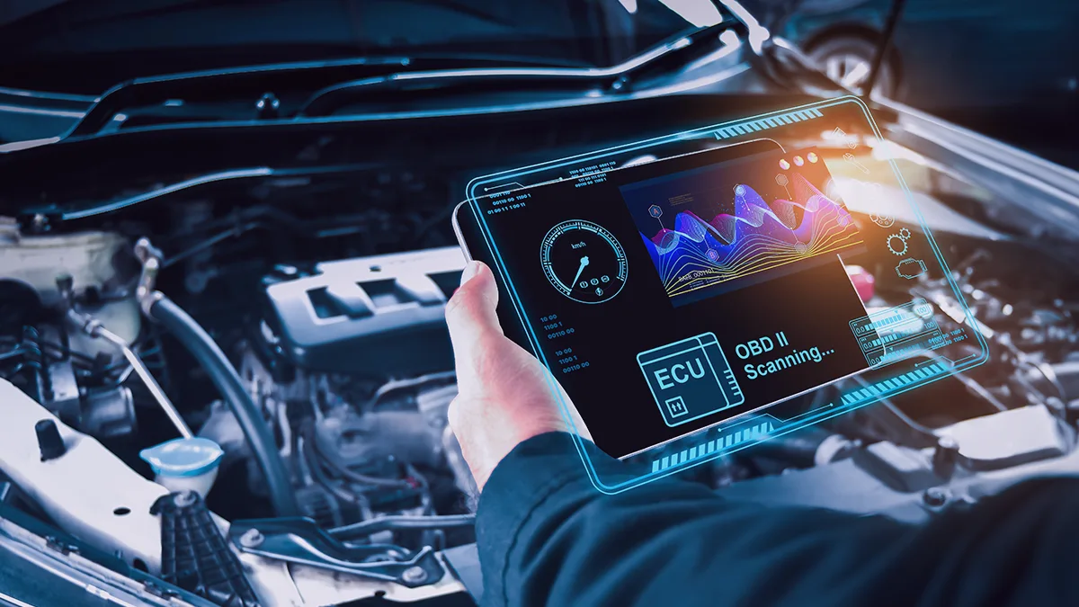Person holding a tablet displaying car engine diagnostics – including graphs, a tachometer, and the text “OBD II Scanning… ECU”; car engine components visible in the background – illustrating advanced diagnostics in digital automotive manufacturing.