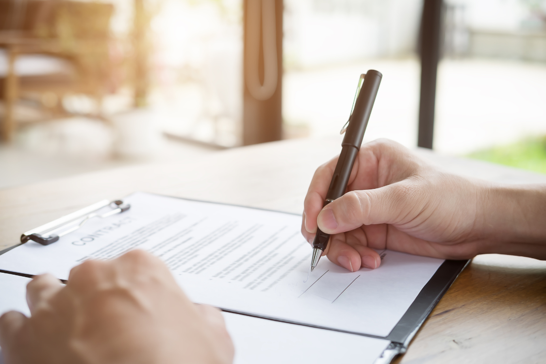 Close-up of a hand signing a confidentiality agreement, a required step before accessing a Confidential Information Memorandum.