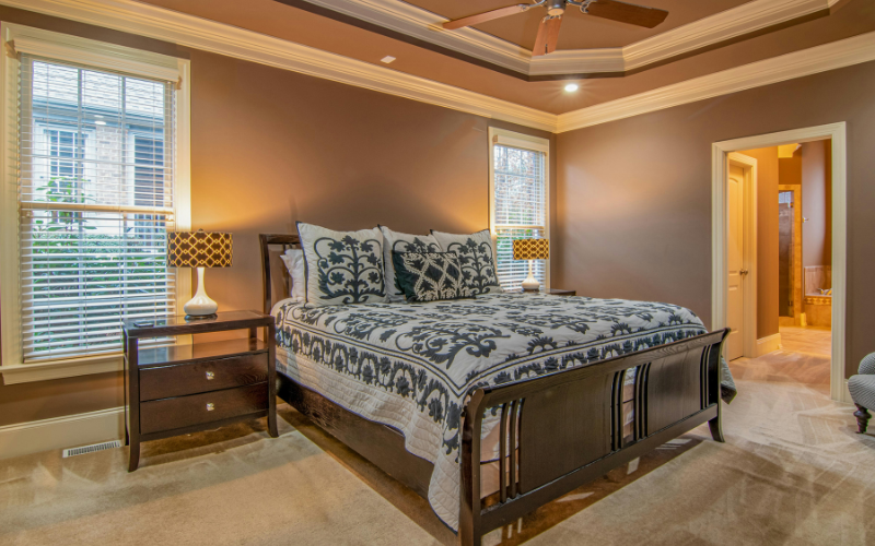 A room with a 5 blade fan, lamps and wooden bed