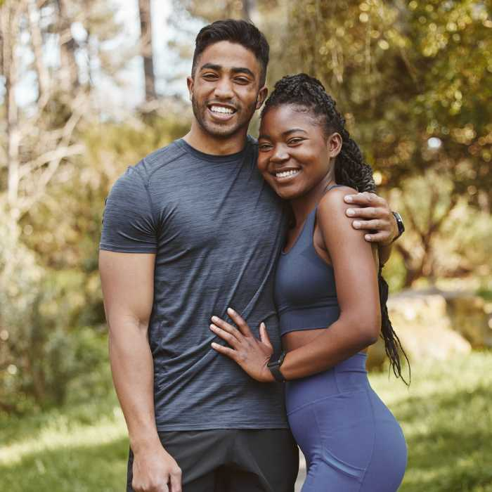 A fit and happy couple, dressed in athletic wear, pose together in a serene park setting, embodying the health and vitality promoted by AIM Companies Supplements, which include ingredients like hibiscus flower, marshmallow root, and Irish moss. Their active lifestyle reflects the brand’s mission to continue improving people's lives, mindful of sensitivities such as allergic reactions to components like psyllium dust. The Good Stuff Health Shop South Africa.