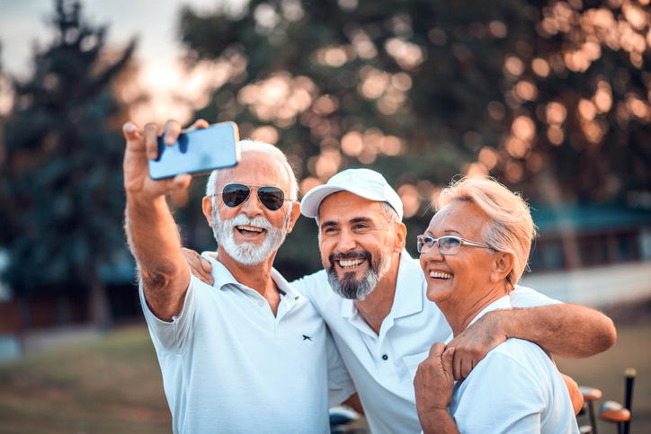 Three cheerful older adults pausing their golf game for a selfie.