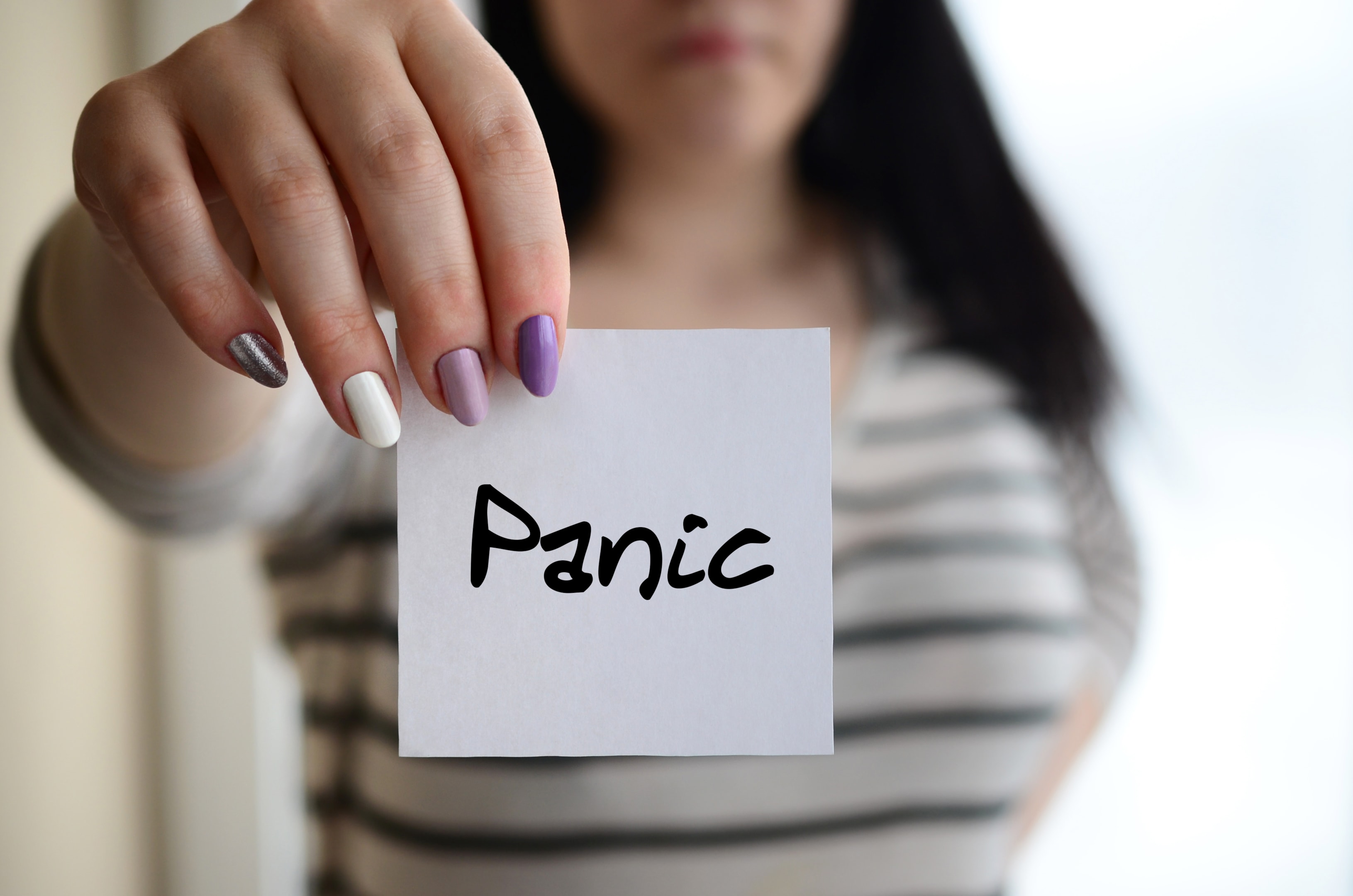 A person holding up a small white note with the word "Panic" written on it, representing the initial recognition required to apply Managing Panic Attacks in The Woodlands