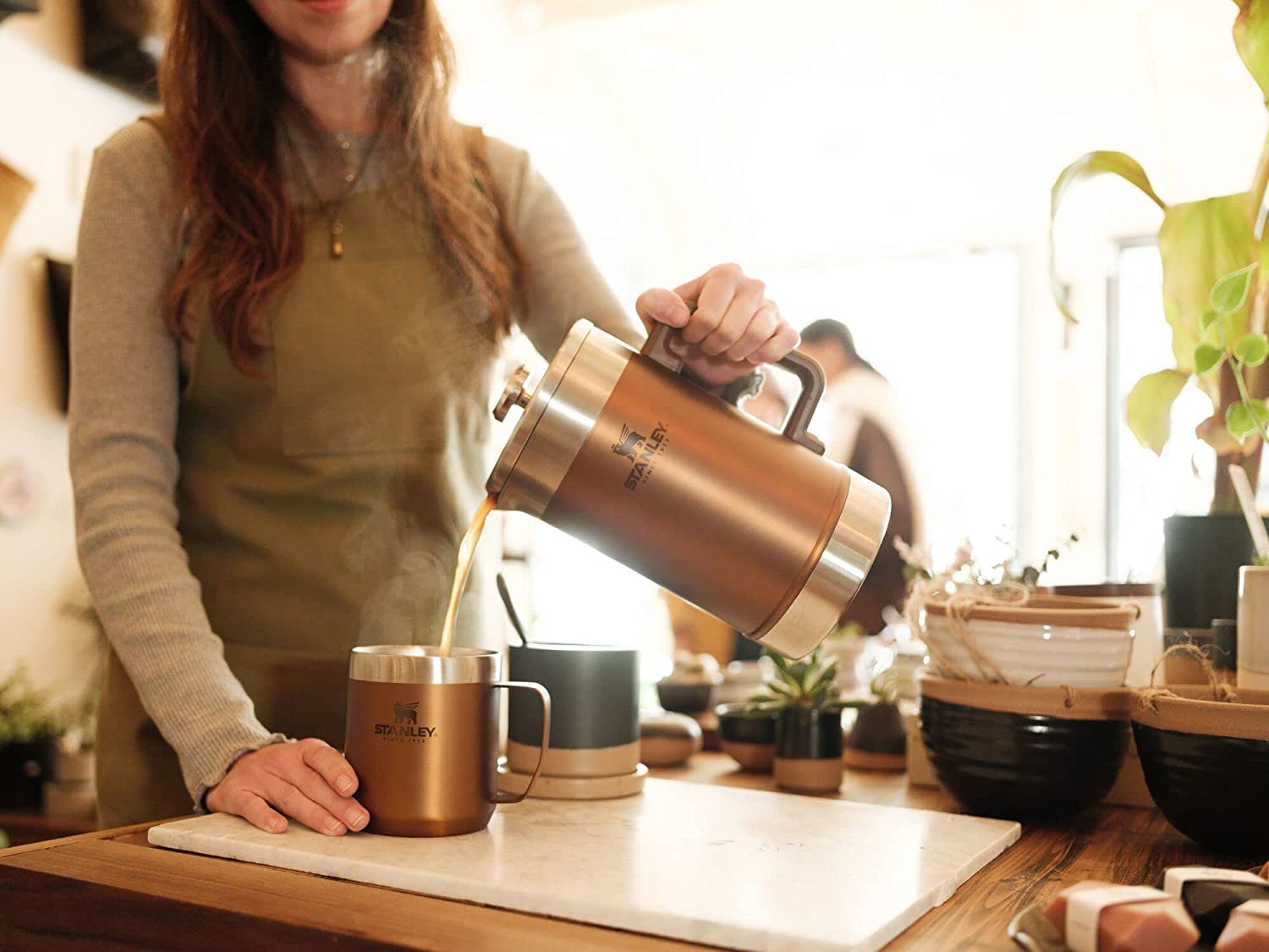 A person holding a Stanley Cup filled with hot coffee, answering the question 'Can you drink coffee in a Stanley Cup?'