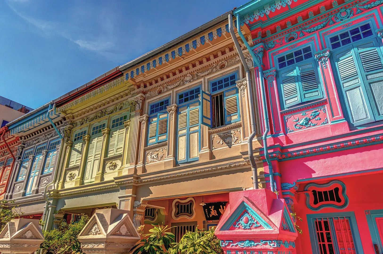 Colorful Peranakan shophouses in Singapore with ornate facades, pastel tones, and intricate window details showcasing traditional Straits Chinese architecture.