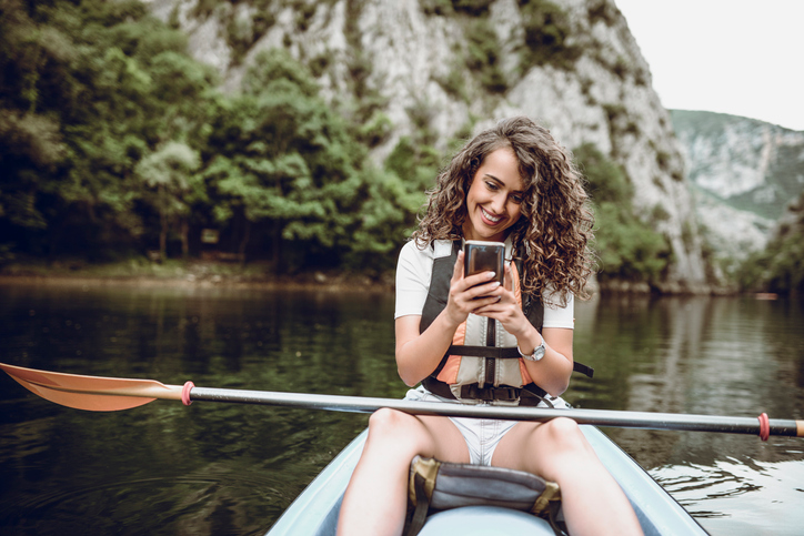 Young woman with curly dark hair sending a text message from a canoe. 