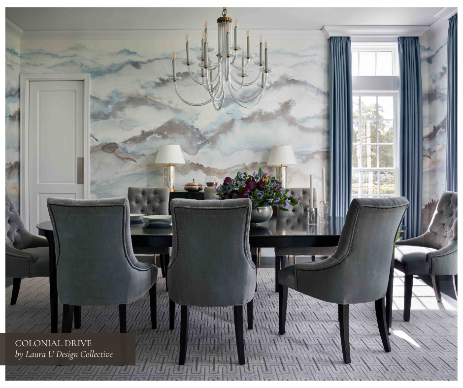 Elegant formal dining room featuring a moody watercolor-style mural, velvet tufted dining chairs in smoky gray, a dark wood dining table, and a graceful chandelier with candelabra lights, framed by soft blue drapes and patterned carpeting.