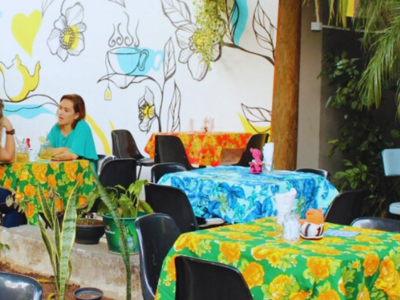 Mesas com forro de chita estampada em área externa e cliente à mesa de cafeteria. Imagem: Reprodução Instagram. 