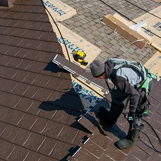 A man installs metal roofing on a house, carefully working on the sloped surface of the roof.