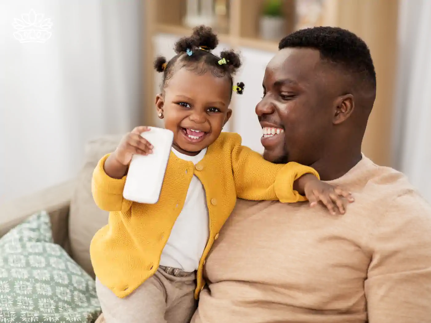 Smiling father holding his happy child who is holding a smartphone, both wearing warm-toned sweaters. Fabulous Flowers and Gifts.