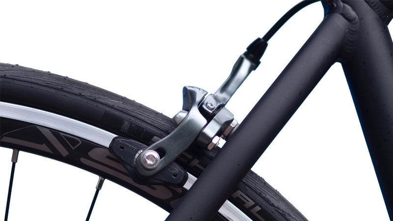 Close-up shot of a black bicycle frame with a matte black finish showing the brakes and part of the tire.
