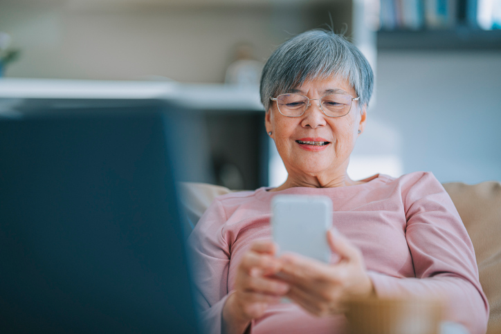 Older woman with short gray hair and glasses using a cell phone. 