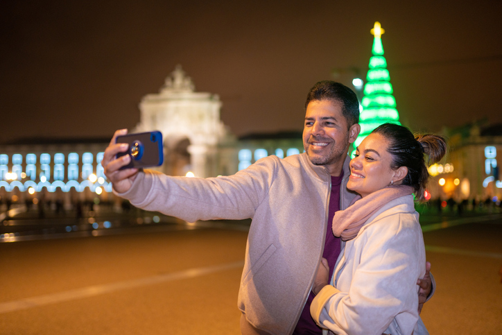 Happy couple snapping a selfie with a Christmas tree in the background. 