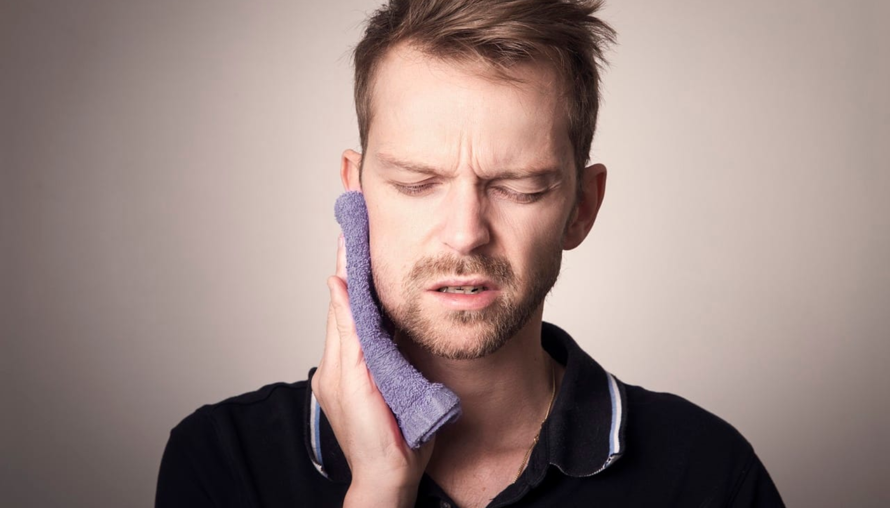 Mann holder kald kompress mot kinnet ved tannverk/hevelse.