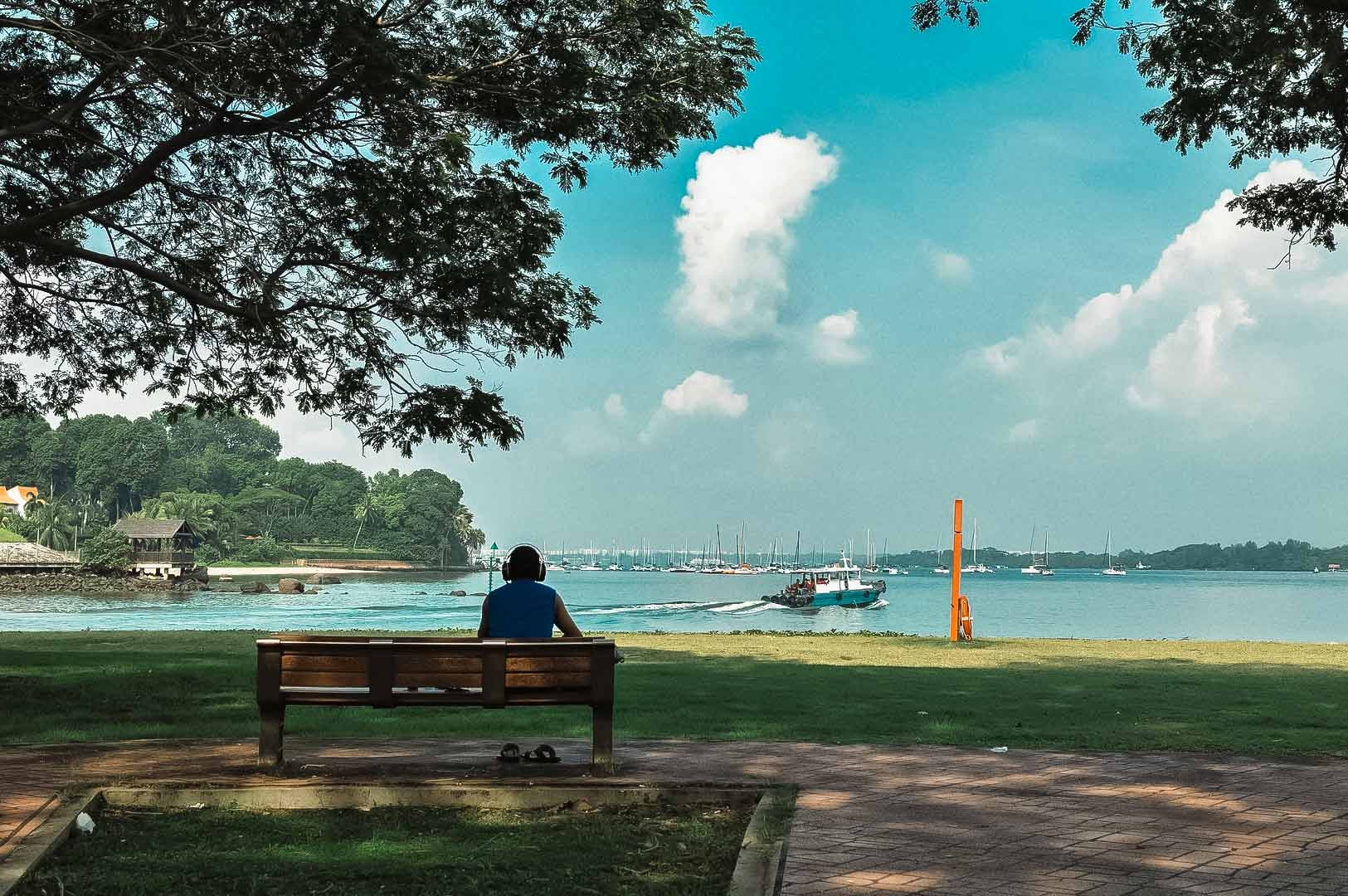 Visitor sitting on a bench at Changi Beach Park overlooking sailboats on the water.