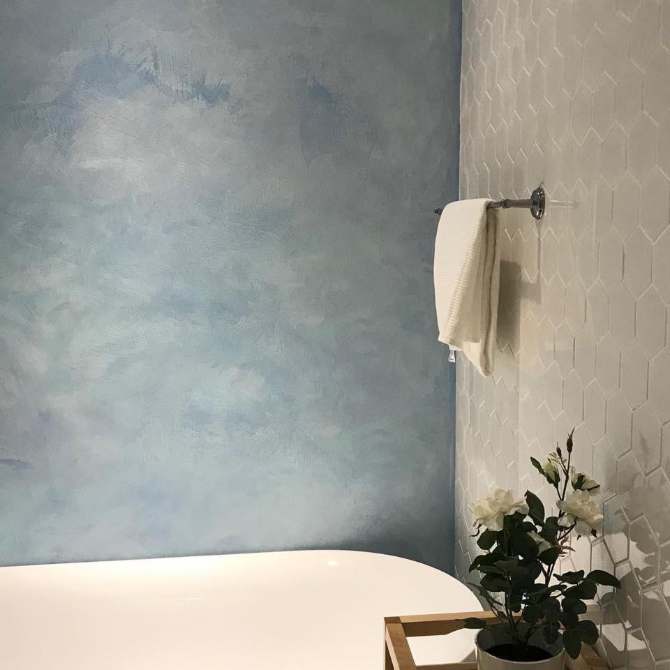 The image depicts a bright, naturally lit room featuring soft matte limewashed walls that showcase texture and color variation, creating an inviting atmosphere. The velvety finish of the limewash paint adds depth to the space, enhancing its overall aesthetic appeal.