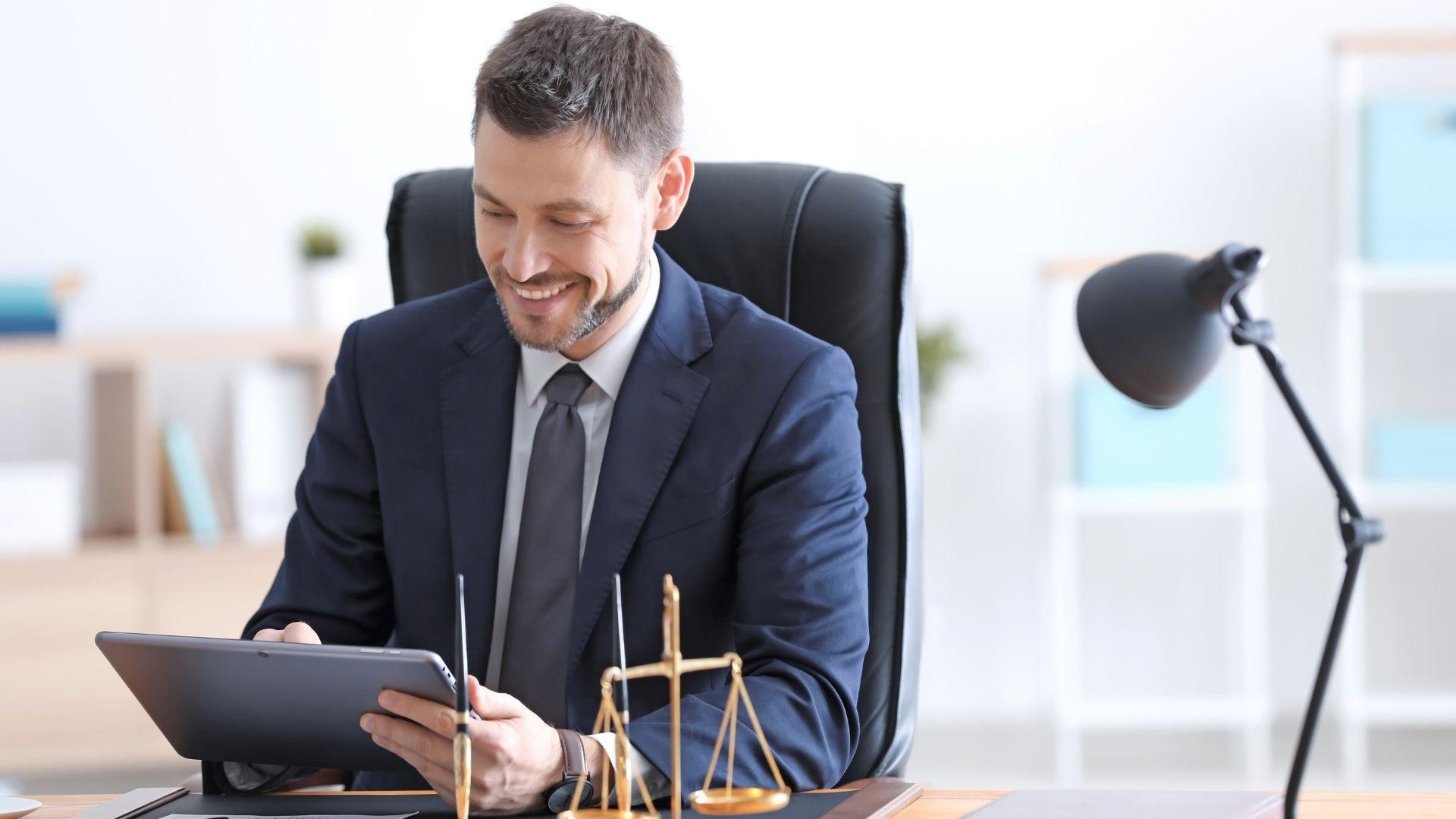 Professional lawyer using a tablet at their desk in a modern office, with legal scales visible in the foreground.