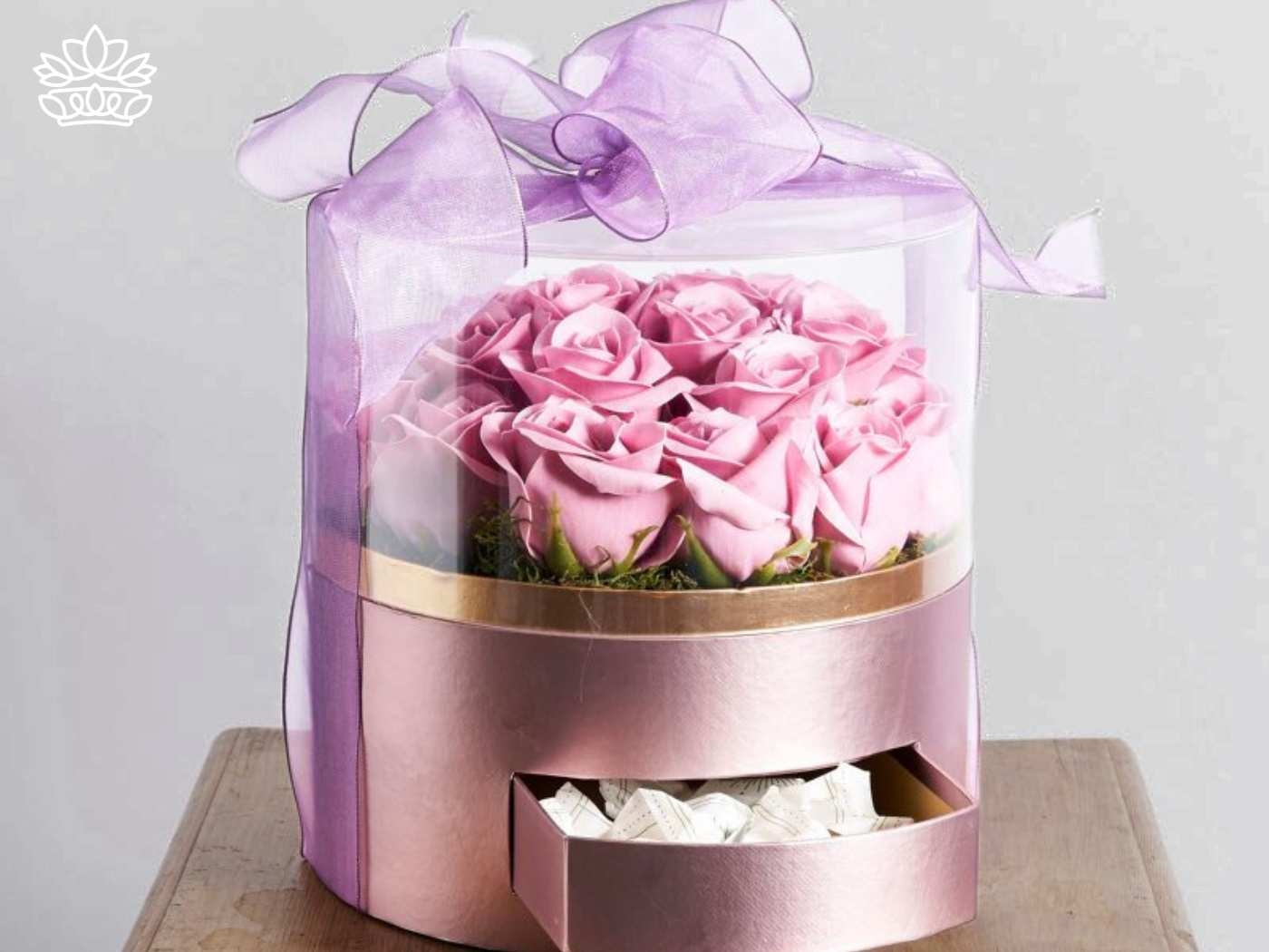 A luxurious gift box filled with elegant pink roses and topped with a sheer lavender ribbon, containing a small drawer of chocolates for a thoughtful, personalized touch. Fabulous Flowers and Gifts. Gifts for Her.
