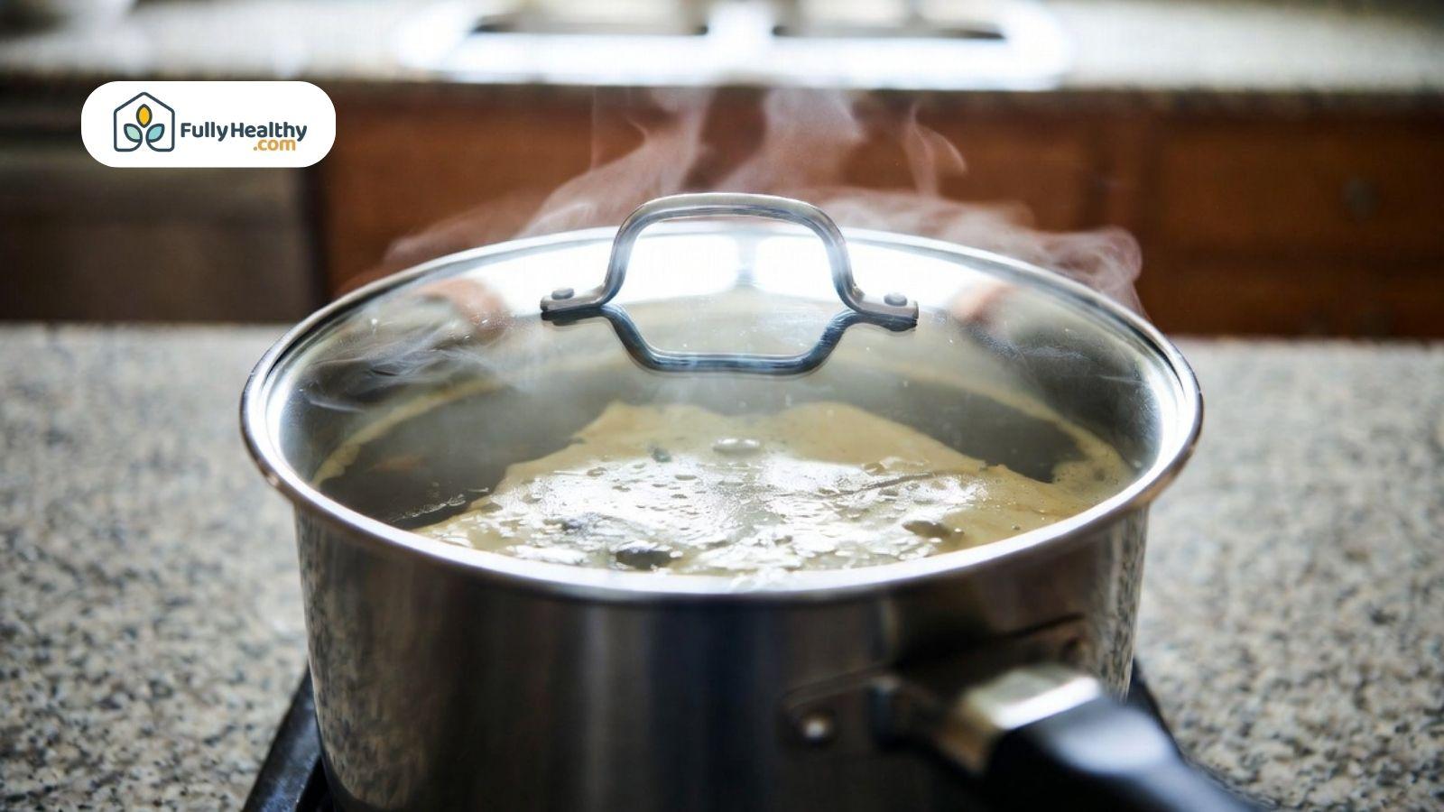 Pot of broth simmering on a stove with steam rising from the lid.