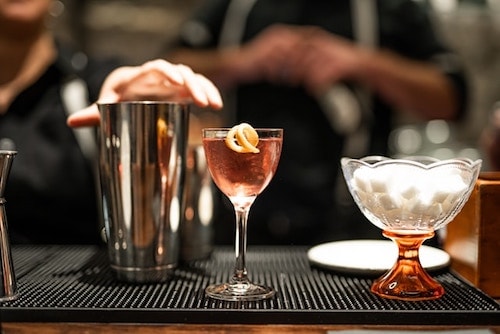 Bartenders proceeding to prepare a craft cocktail in a chilled glass