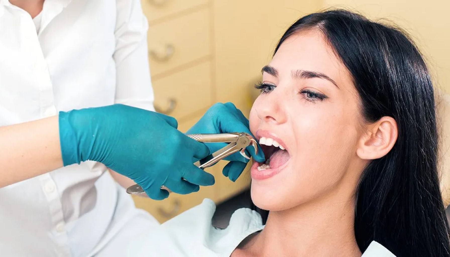 Trekke Tann: Når Det Ikke Lenger Er Noe Å Redde (Men Alt Å Vinne) 14 Tannlege med blå hansker trekker en tann ut av munnen til kvinne som sitter i tannlegestol i lyst rom.