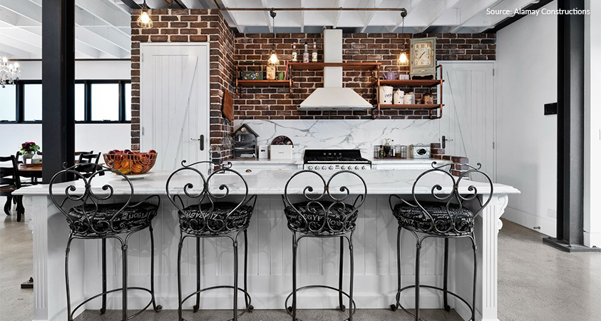 This industrial style kitchen features marble counters, barnyard doors, copper pipe shelves and wrought iron chairs. Photo sourced from Alamay Constructions.