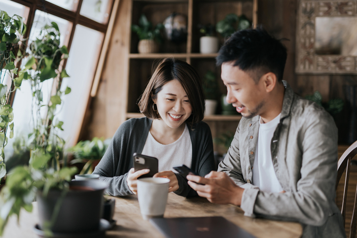 Young couple having coffee and smiling looking at their phones. 
