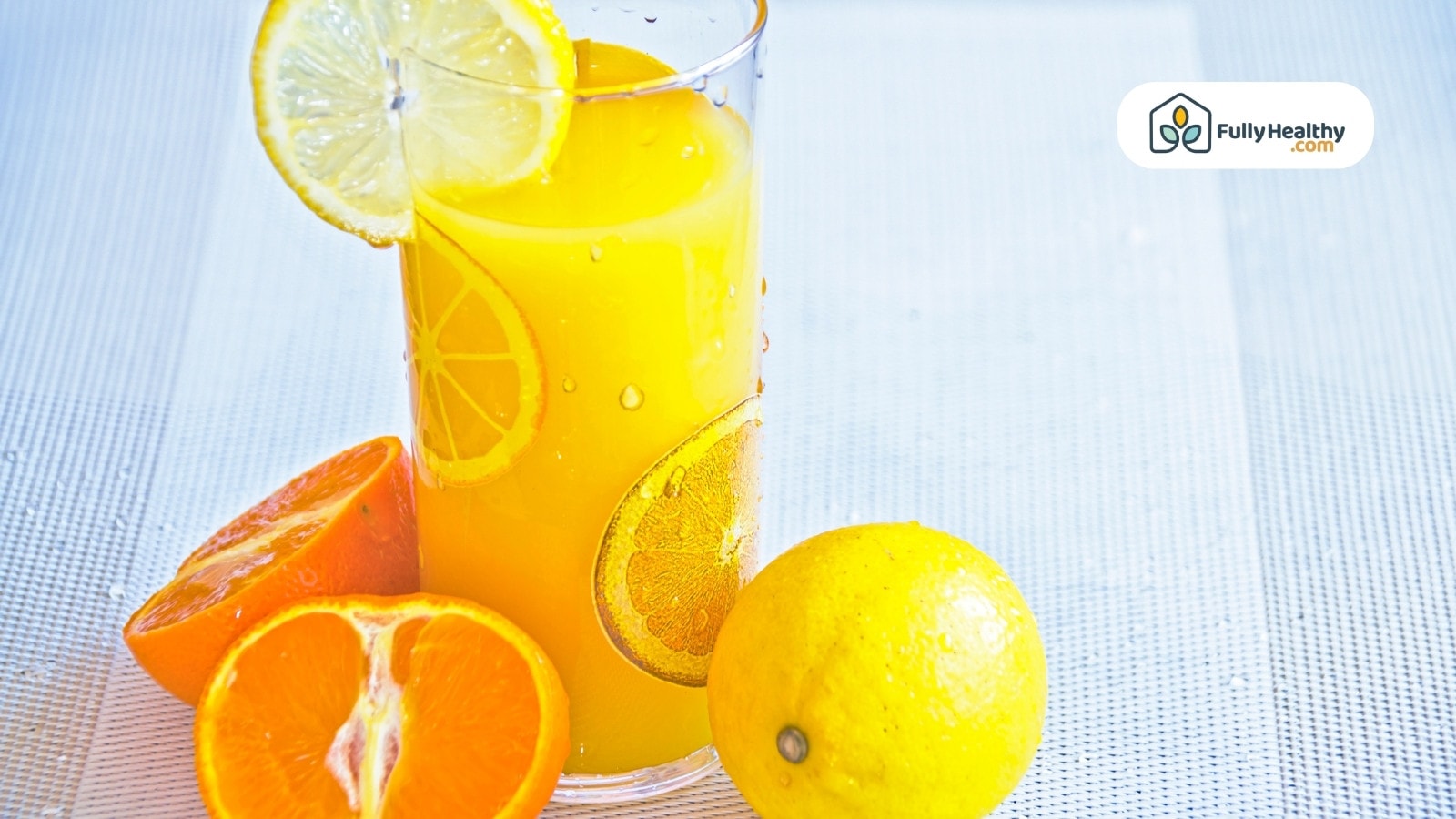 Glass of orange lemon juice with fresh fruits on white surface
