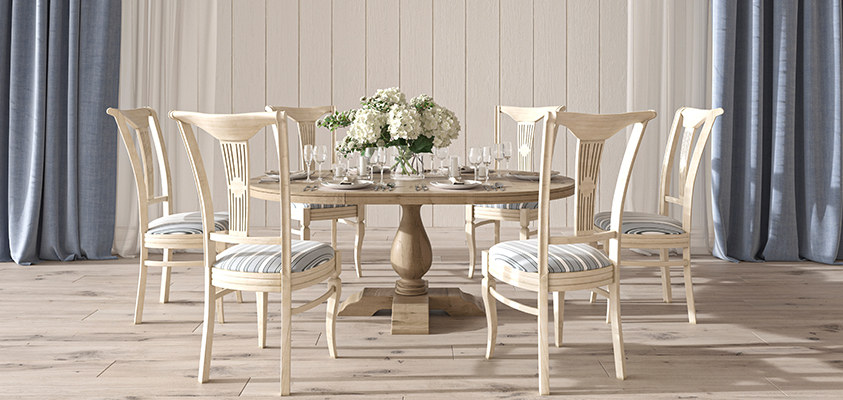 This costal style dining room features the signature Hamptons light timber flooring and beige shiplap walls with blue floor-to-ceiling curtains. The round timber dining table features a display of flowers and tableware, and the surrounding chairs feature wooden frames accented with blue and white striped seat cushions.
