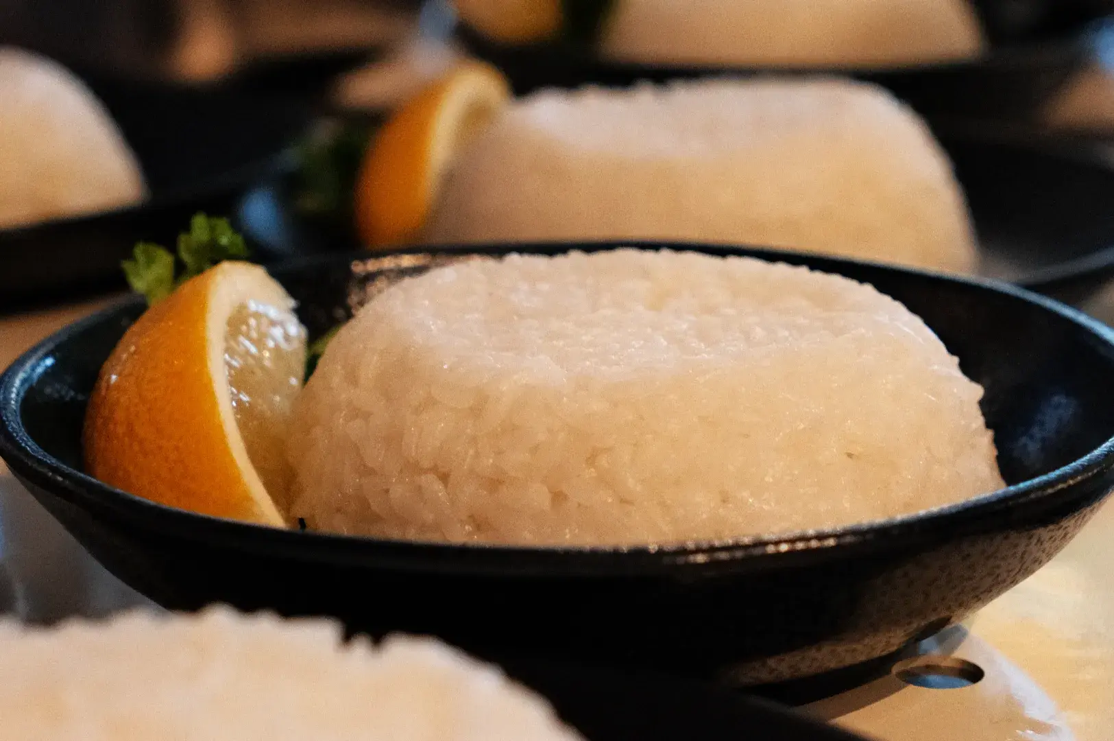 A bowl of white rice with a slice of lemon and a piece of green garnish.