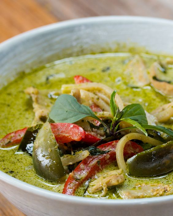 Thai green curry served in a bowl with vibrant green sauce, accompanied by vegetables and herbs.
