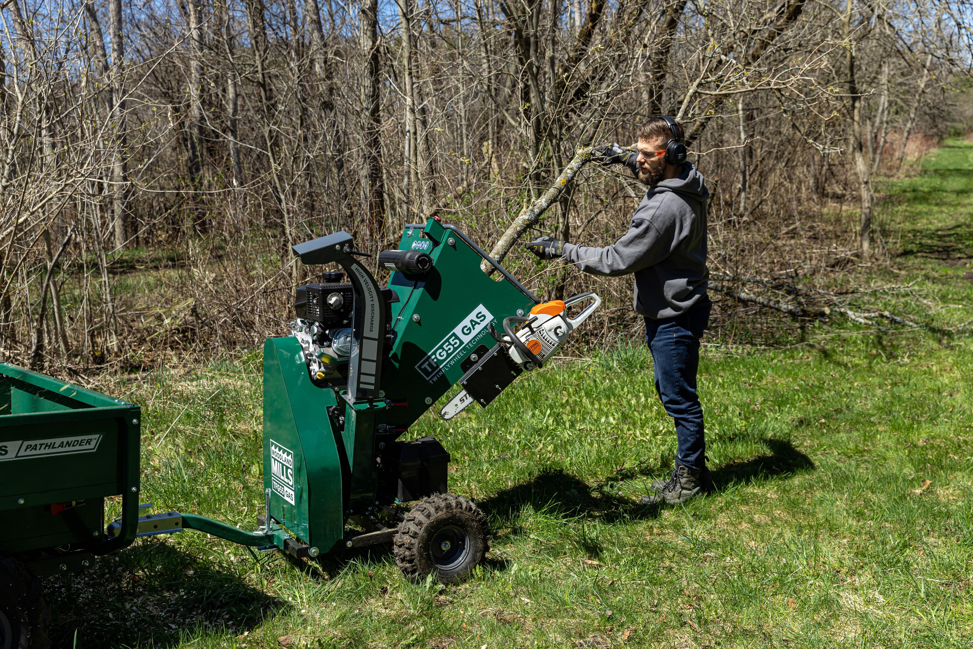 A man feeding a whole tree into a Woodland Mills TFG55 GAS Wood Chipper.