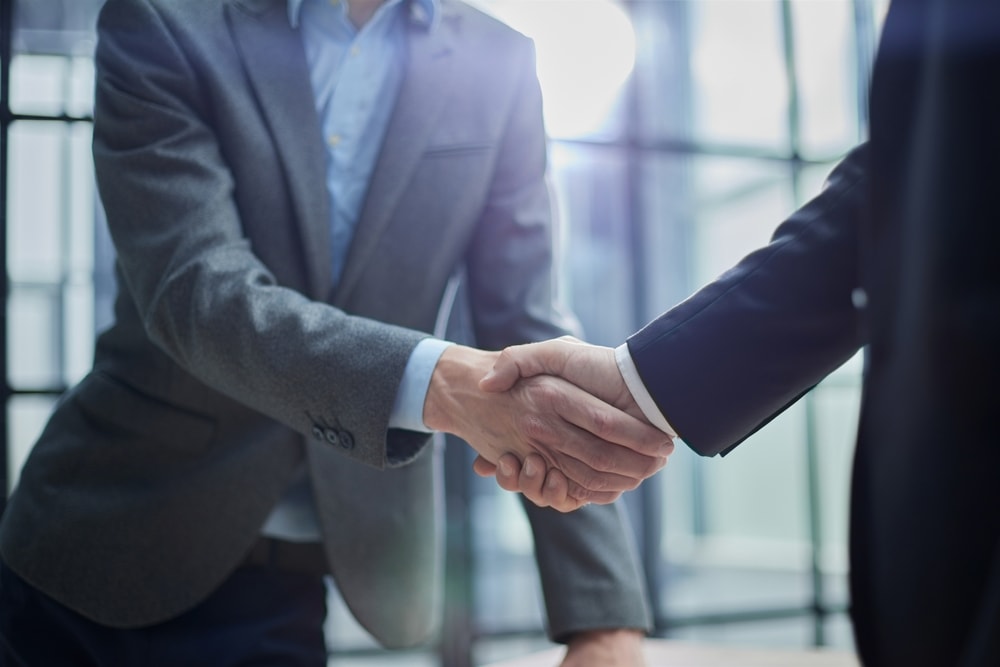 Dwóch mężczyzn w garniturach podaje sobie rękę na powitanie w biurze, symbolizując podpisanie umowy o pracę lub nawiązanie współpracy.