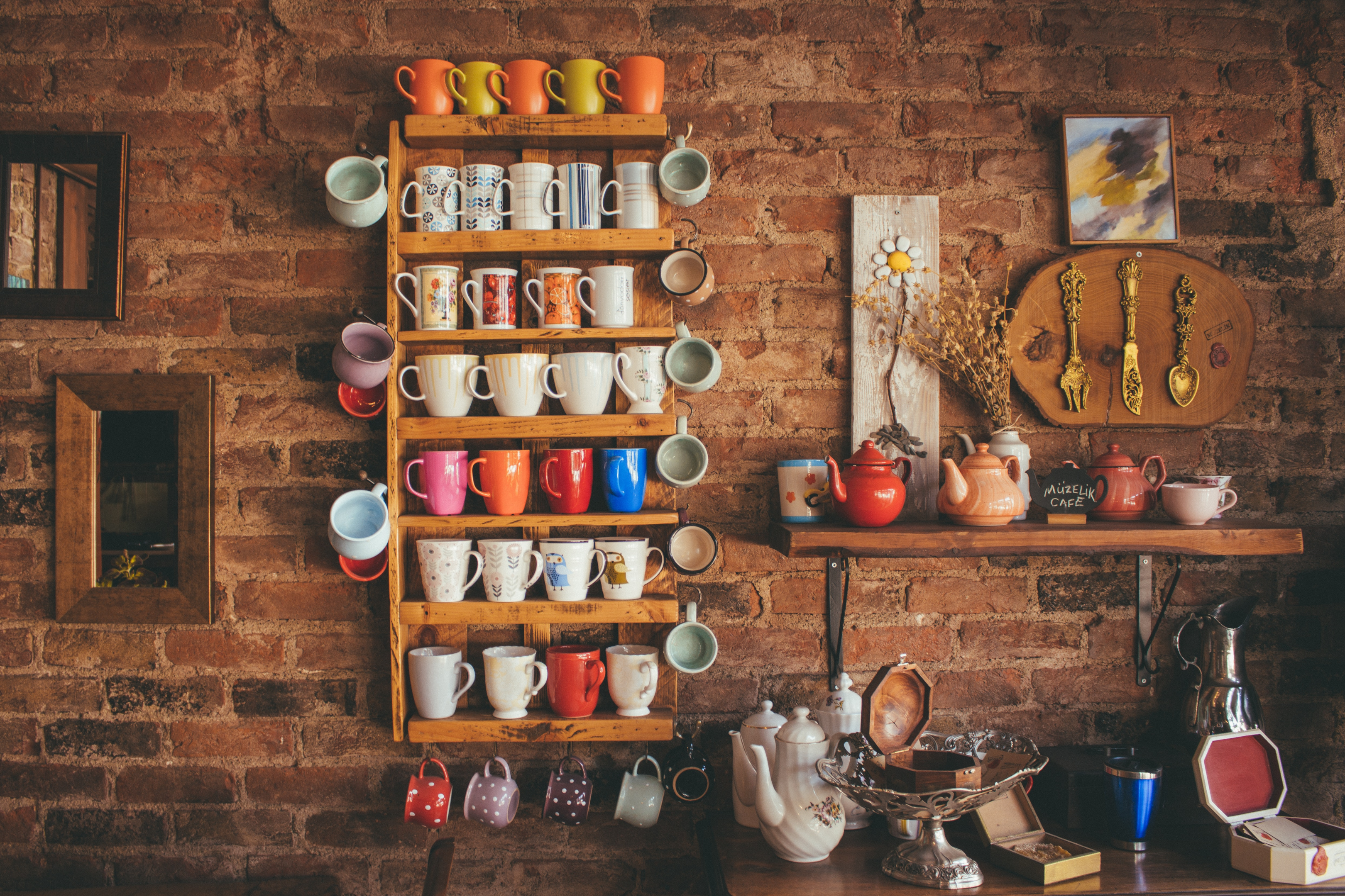 assorted color mugs on wooden shelving against brick wall