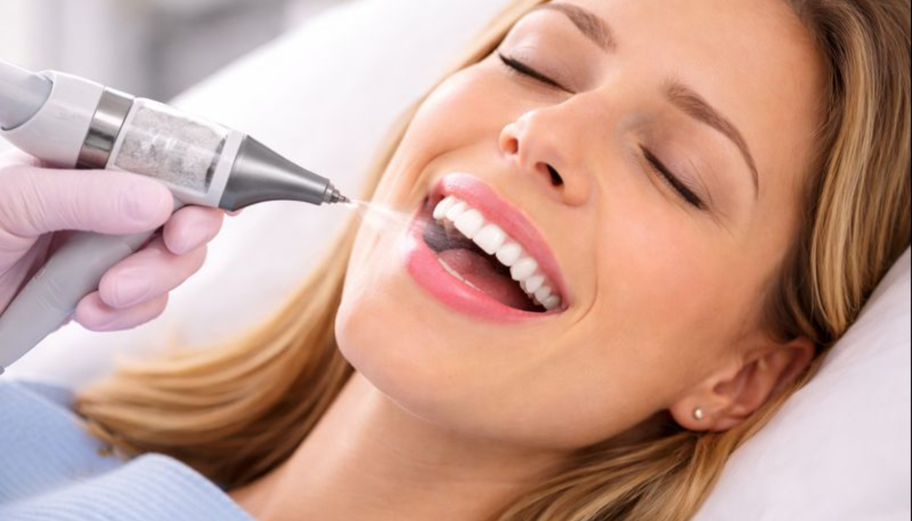 Pasient får skånsom tannrens med AirFlow hos tannpleier, med avslappet uttrykk og rene, lyse tenner.