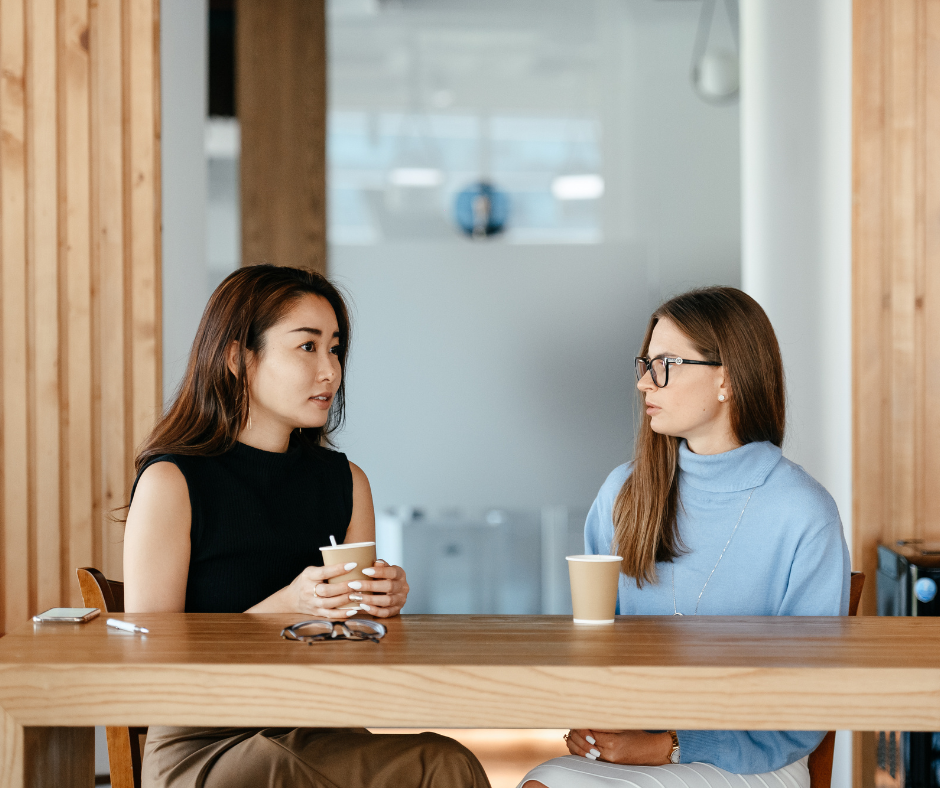 two women sit at a cafe table talking