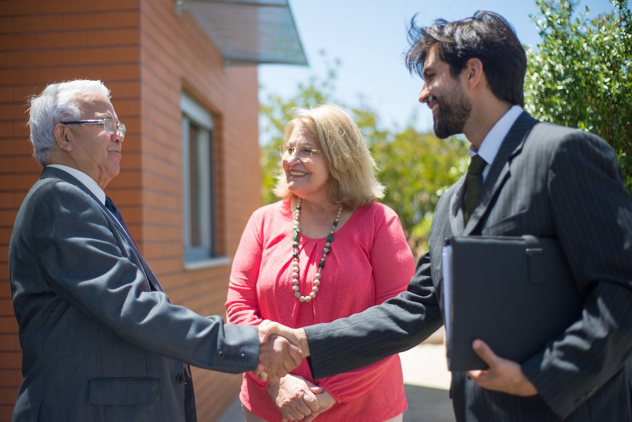 Friendly property manager shaking hands with a happy elderly couple.