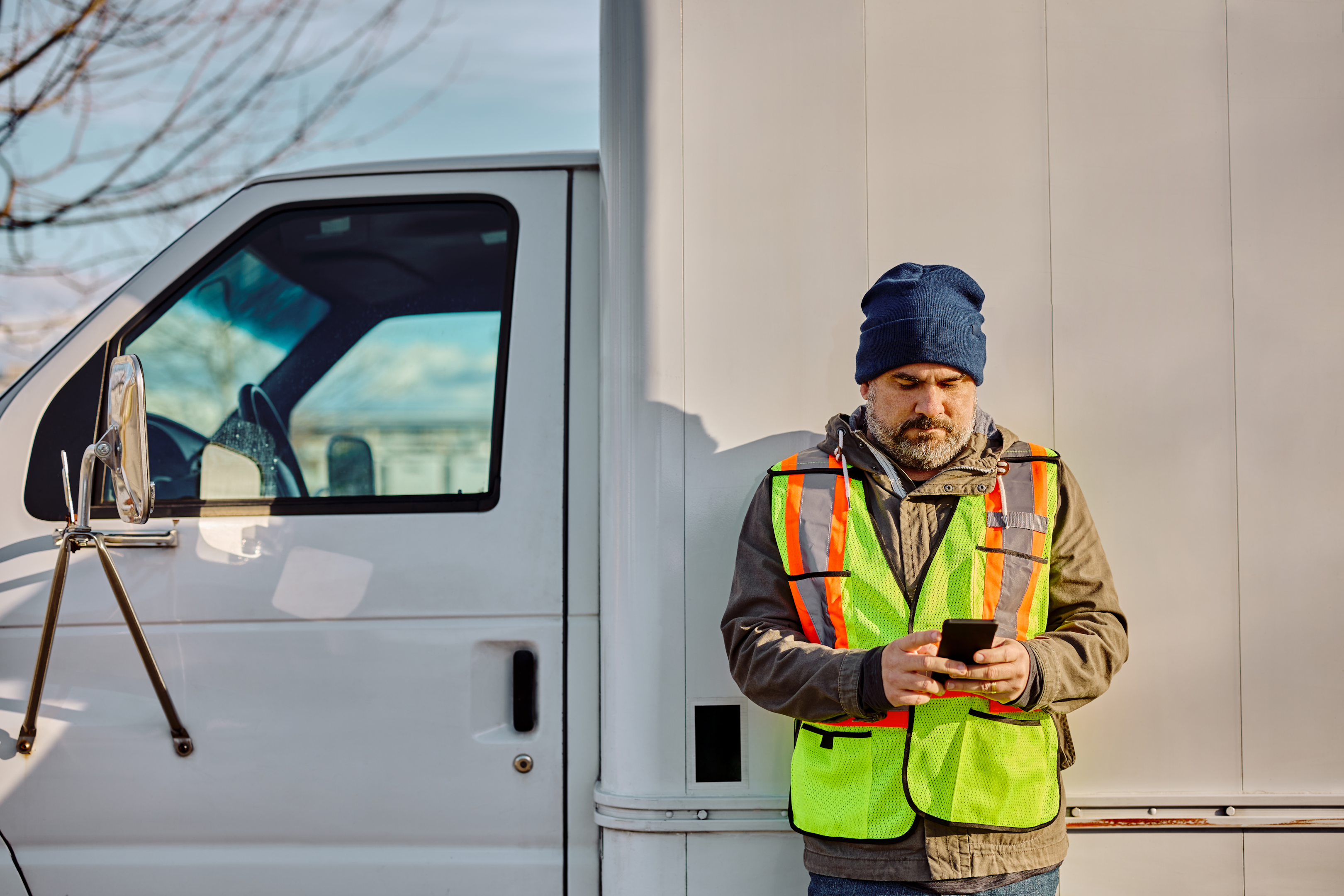 A driver standing by his truck looking at his phone