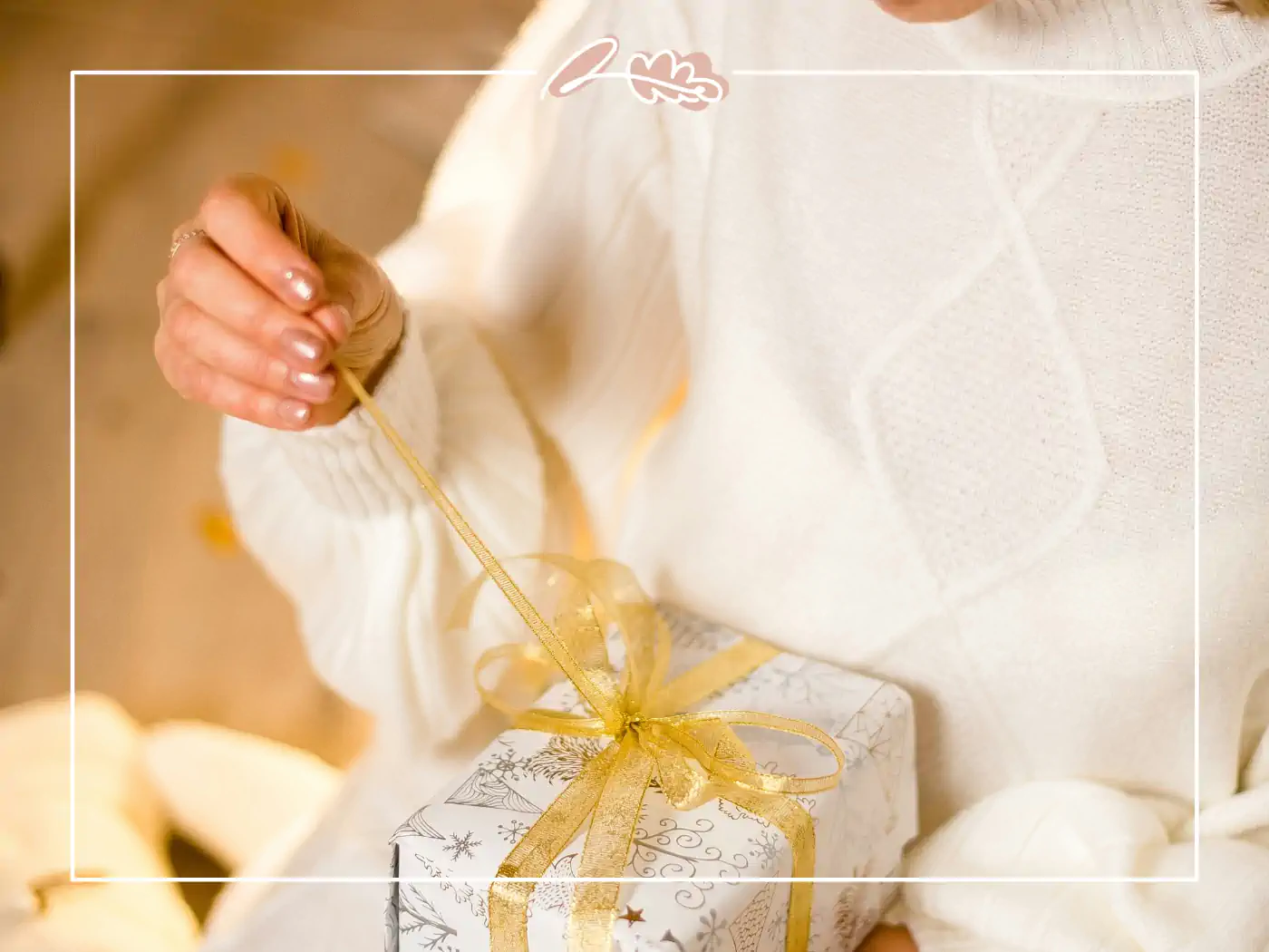 Person in a white sweater holding a white gift box with a golden ribbon - fabulous flowers and gifts